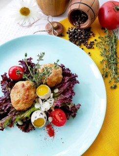 A blue plate with a salad topped with meatballs, quail eggs, tomatoes, and herbs arranged