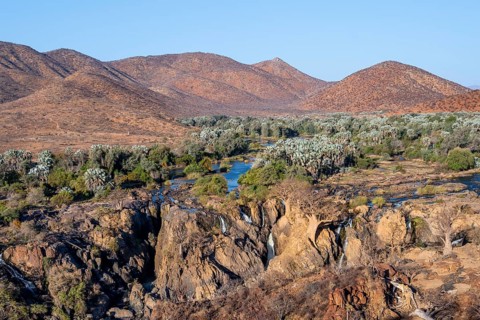 Kunene River with green vegetation in dry red mountain landscape, waterfall and African Baobab