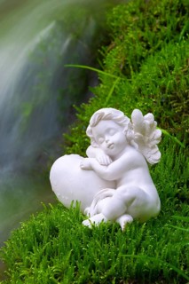 Porcelain angel figurine on moss by a waterfall