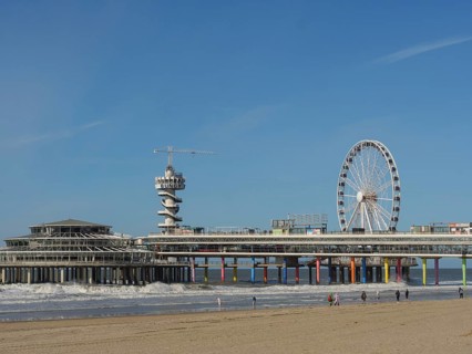 Pier with Ferris wheel and tower on the beach, people walking along the beach, parasols and a pier