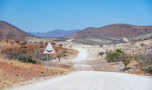 Road with road sign Attention river crossing, gravel track leads through barren dry landscape with
