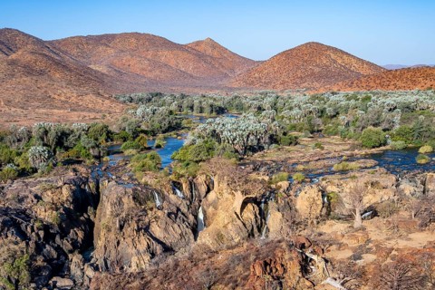 Kunene River with green vegetation in dry red mountain landscape, waterfall and African Baobab