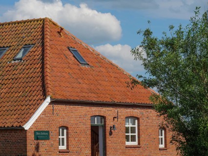 A brick house with a red tiled roof and windows under a blue sky, Baltrum Germany