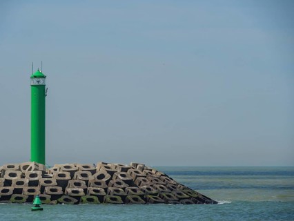 A single green lighthouse next to concrete breakwaters with calm sea in the background, lighthouses