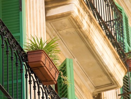 A balcony with decorative lattices, green shutters and a flower pot on a beige-coloured facade,