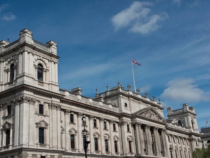 Large historic building with a waving Union Jack flag on the roof, against a cloudy sky, London,