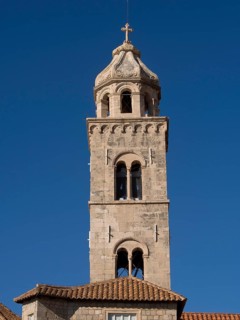 High stone church tower with a cross at the top, in front of a bright blue sky, the old town of