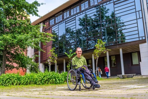 Full length portrait of a cacuasian adult man with cerebral palsy sitting in electric wheelchari in