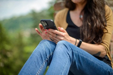 Young woman in casual clothing focused on conversation with smartphone in a peaceful garden with