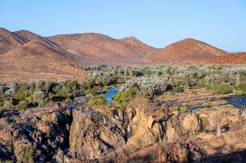 Kunene River with green vegetation in dry red mountain landscape, waterfall and African Baobab