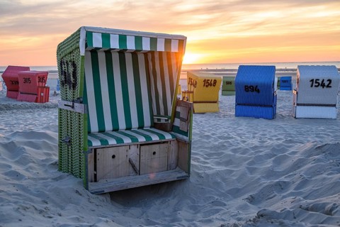 A green beach chair in a sand pit, surrounded by colourful beach chairs, at sunset, summer evening