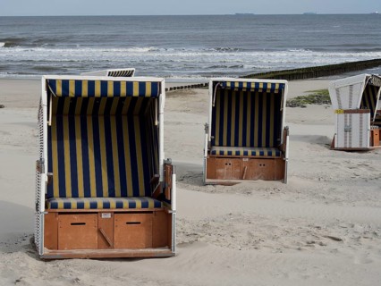 Three beach chairs with striped awnings stand on the beach in front of the sea under a slightly
