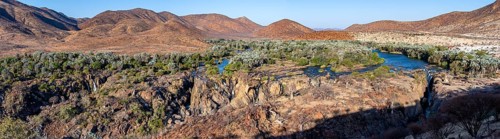 Panorama, Kunene River with green vegetation in dry red mountain landscape, waterfall and African