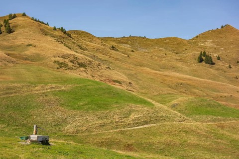 Abandoned hut on rolling green hills under a clear sky, rural and peaceful surroundings, mountain