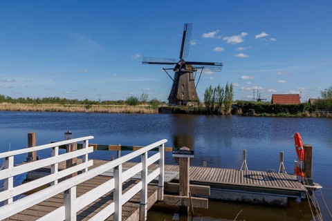 Wooden walkways on a river with an old windmill and clear sky in the background, windmills of