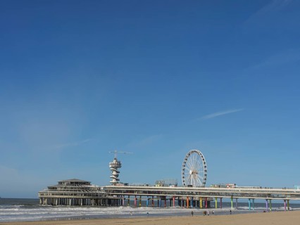 Pier with Ferris wheel and tower on the beach, sea in the background under a blue sky, parasols and