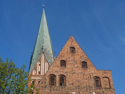 Church tower and gable of a brick gothic church with trees and blue sky in the background, red