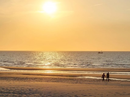 A family walks on the beach during a warm sunset, the sea is calm, sunset on the beach of de haan