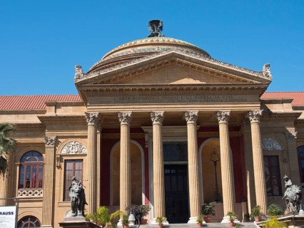 Historic theatre building with imposing columns and richly decorated capitals under a clear blue