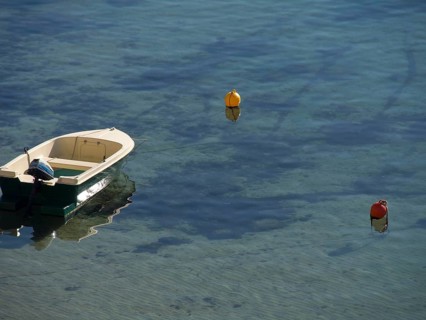 A small boat floats on clear water surrounded by buoys that are reflected in the water, the old