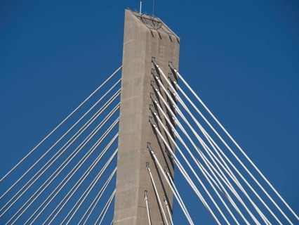 Modern cable-stayed bridge with a high concrete tower and numerous steel cables under a clear sky,