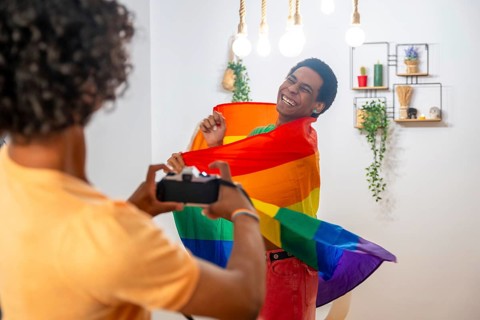 Gay man wrapping with lgtb flag while couple taking photos of him at home
