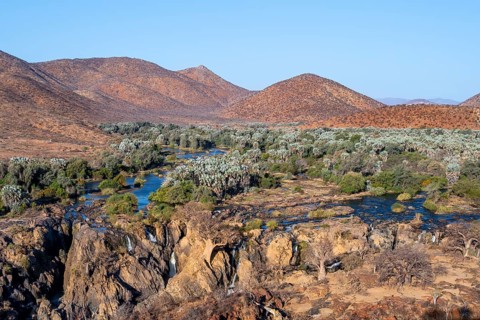 Kunene River with green vegetation in dry red mountain landscape, waterfall and African Baobab