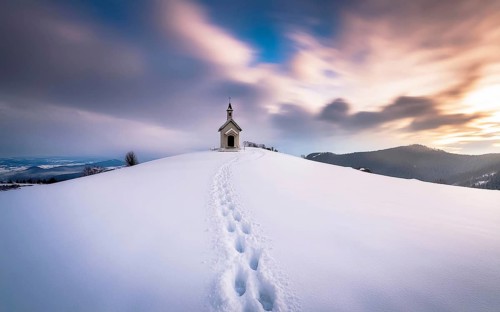 Footprints in fresh snow on a hill to a small chapel backlit in winter, AI generated, AI generated