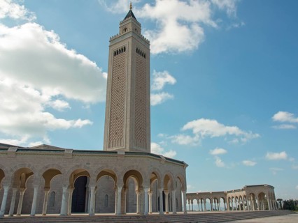 Large mosque with high minaret and arches under a cloudy sky, Tunis in Africa with ruins from Roman