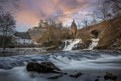 Beautiful landscape in winter with ice and snow. Waterfall of the river Elz near the castle