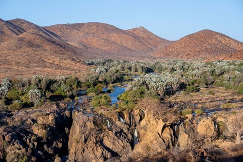 Kunene River with green vegetation in dry red mountain landscape, waterfall and African Baobab