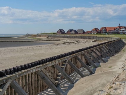 A beach with wooden constructions and houses in the background, sea and sky with some clouds,
