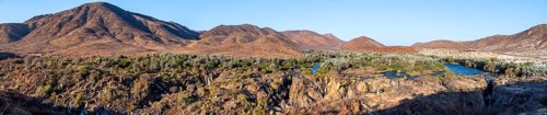 Panorama, Kunene River with green vegetation in dry red mountain landscape, waterfall and African