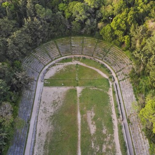 Aerial view of an ancient semicircular stadium with rows of stone seats surrounded by forest,
