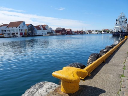 Waterfront with a yellow bollard and tyre protection, water and city in the background, in sunny