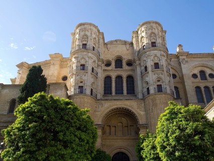 A historic cathedral with two towers and stone facade surrounded by trees on a sunny day, The city
