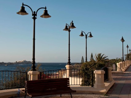 Promenade along the sea with benches, decorative lamps and palm trees, railings and clear sky,
