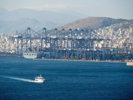 A large harbour with ships and containers, behind it a city and mountains, ancient buildings with