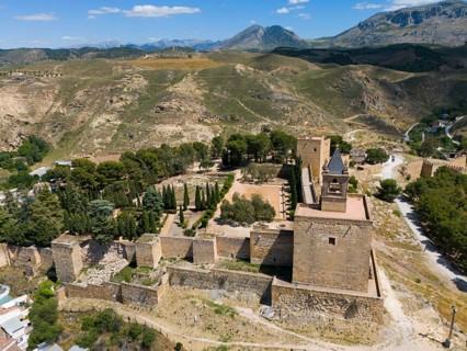 Aerial view of a historic fortress, surrounded by trees and mountains, with impressive walls and