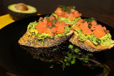 Gourmet bruschetta topped with avocado and salmon on a black plate, garnished with fresh dill
