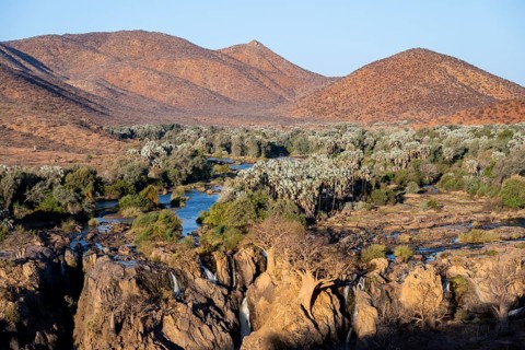 Kunene River with green vegetation in dry red mountain landscape, waterfall and African Baobab