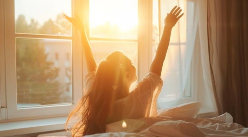 A woman is in bed, smiling and stretching her arms after waking up at sunrise early morning, AI