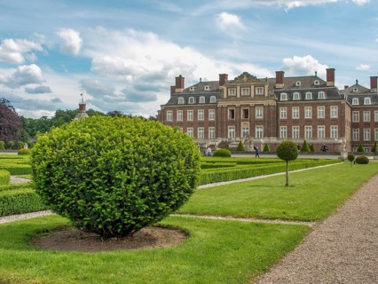 Well-kept symmetrical garden with hedges and paths in front of a historic castle under a cloudy