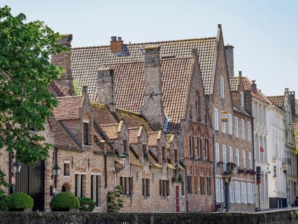 Medieval brick buildings with several chimneys along a canal, surrounded by trees, historic houses