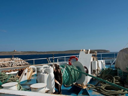 A fishing boat in the harbour with ropes and equipment, an island in the background under a clear