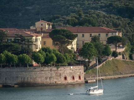 Yellow building on the waterfront, a sailboat in the foreground and forest covered hills in the