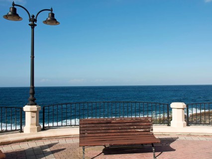A wooden bench in front of a metal railing with sea and sky in the background, Valetta, Malta,