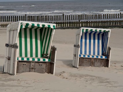 Two beach chairs, one green and white and the other blue and white striped, in front of a calm sea