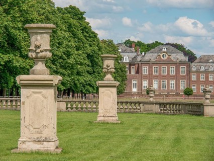 Two stone sculptures on lawn in front of an impressive historical building, surrounded by trees and