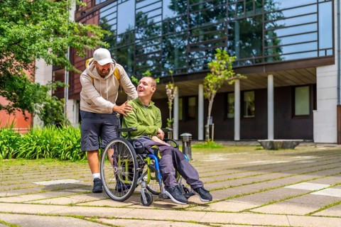 Full length photo of a caucasian adult man with special needs and friend walking along the